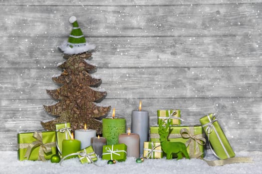 Shabby chic green and white christmas decoration on grey wooden background with snowflakes and candles.