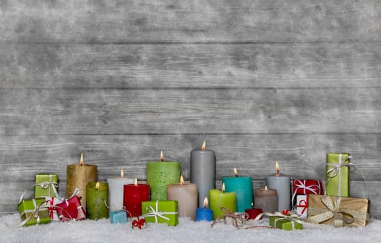 Colorful christmas decoration with different candles on grey and white wooden snowy background.