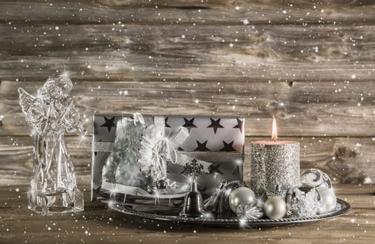 Silver and beige christmas decoration with present, angel and burning candle on wooden background.