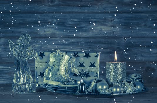 Dark blue christmas decoration with candle and presents on wooden background with a glass angel.