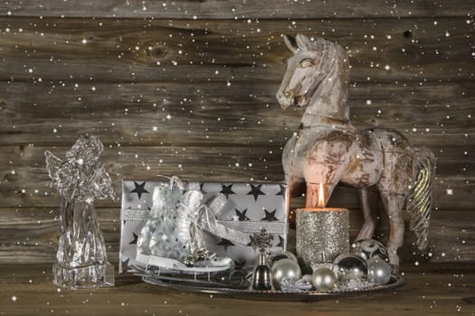 Silver and beige christmas decoration with present, angel, horse and burning candle on wooden background.