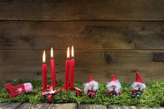 Four red burning christmas candles on wooden background with green moss and brownies.