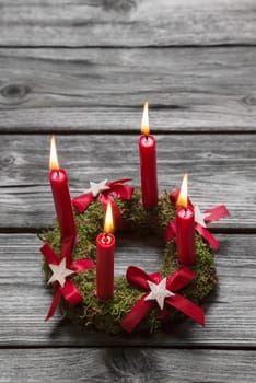 Greeting card with four red burning advent candles on wooden grey background.