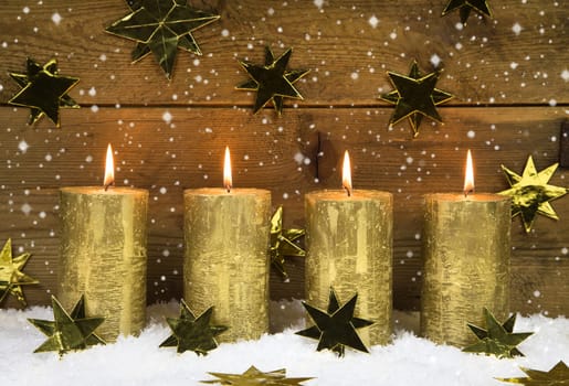 Four golden burning candles for christmas on wooden rustic background.
