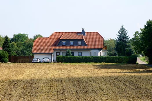 The photograph of a detached house behind a ploughed field.