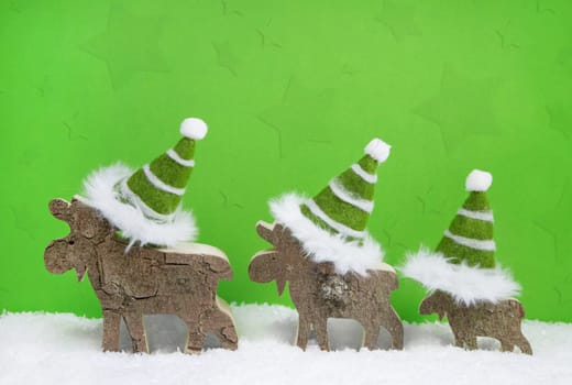 Handmade reindeer family on green and white wooden christmas background with santa hats.