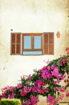 Catalan window with open wooden shutters, decorated with pink flowers