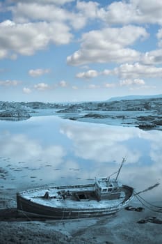 old fishing boat beached on a coastal beach in county Donegal, Ireland in blue tone