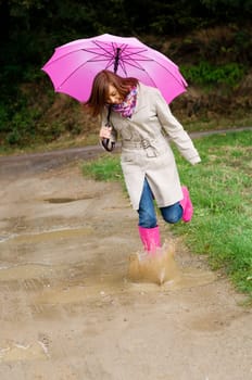 Young woman with rubber boots jumping in puddle