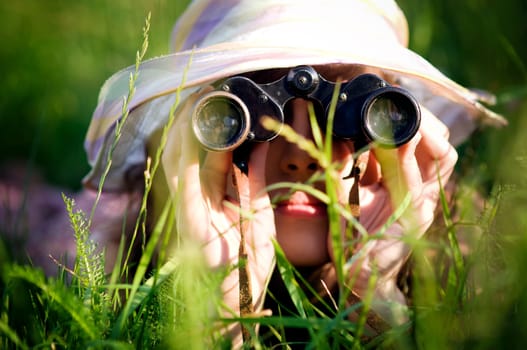 Young woman looking through binoculars in grass