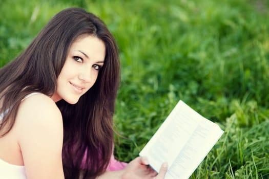 Young woman reading a book on meadow