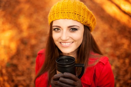 Beautiful young woman drinking hot drink in park