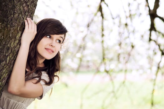 Beautiful young woman hiding behind tree trunk
