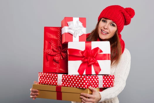 Smiling young woman in winter hat holding a lot of christmas gifts