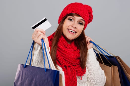Smiling woman in winter clothes showing credit card and holding shopping bags
