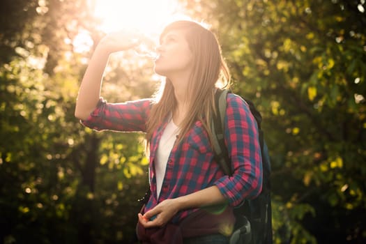 Beautiful female hiker drinking water in forest at sunset