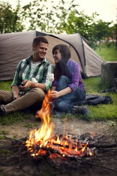 Young couple sitting near a campfire and toasting marshmallow