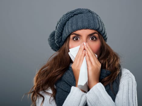 Young woman wearing warm hat sneezing