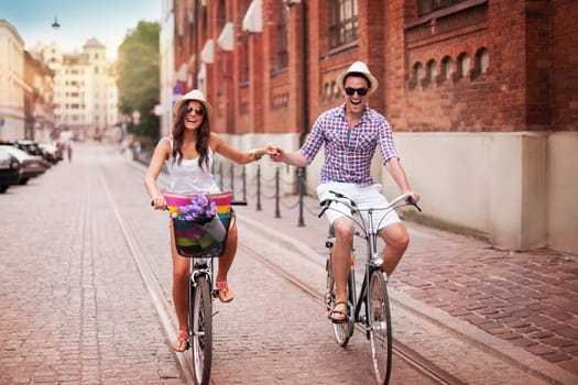 Happy young couple holding hands and riding on bike