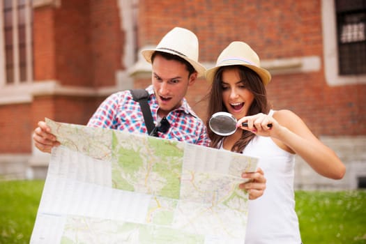 Shocked couple looking at map through magnifying glass