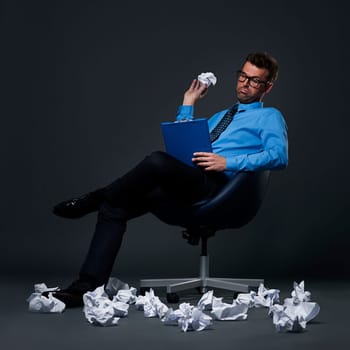 Sitting businessman throwing a crumpled paper with bad ideas on the floor