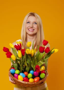 Happy woman holding basket with spring flower and easter eggs