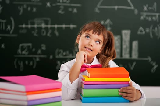 Cute little schoolgirl sitting in classroom with her books and dreaming