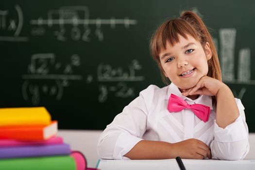 Cute little schoolgirl sitting in classroom with her books