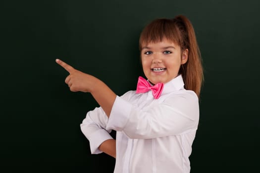 Smiling girl with pink bow tie pointing at copy space