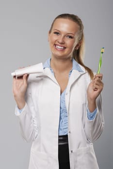 Young female dentist with beautiful smile holding toothbrush and toothpaste