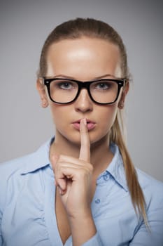 Serious woman wearing glasses showing quiet hand sign