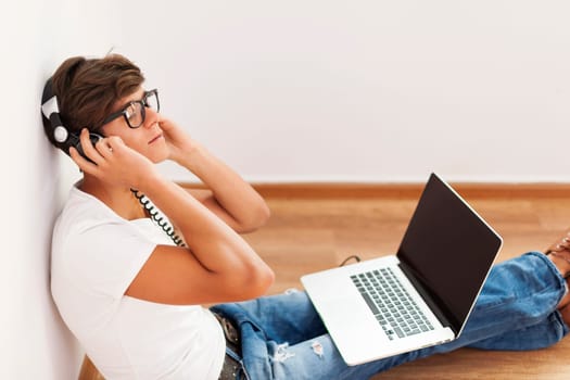 Handsome hipster sitting up against wall listening to music