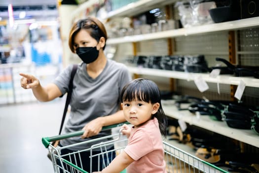 Cute boy standing in the shopping cart and doing grocery shopping with his mother.