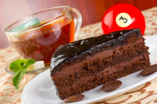 Portion of chocolate cake and cup of tea with fresh mint, served on a white plate