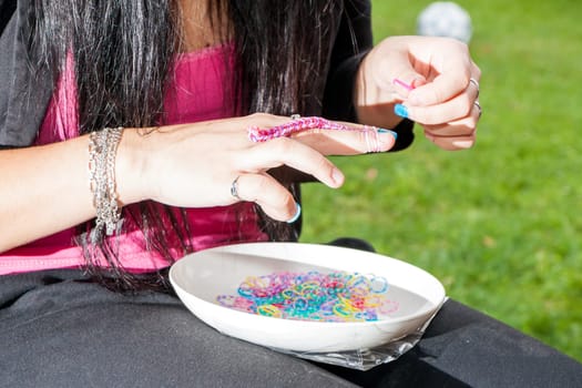 Girl with colorful nails making a rubber loom bracelet with a hook . Hands close up. Young new modern fashion concept.