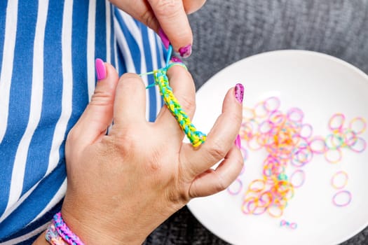 Women with colorful nails making a rubber loom bracelet with a hook . Hands close up. Young new modern fashion concept.