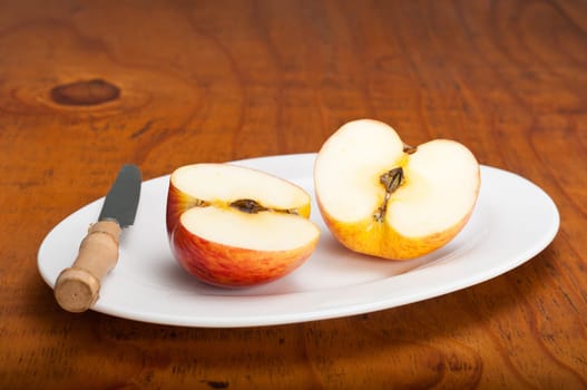 Delicious fresh apple cut in half on a white plate on a wooden table