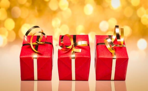 Photo of three red and gold gift boxes with out of focus lights on a golden background