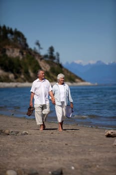 Vertical, outdoor photo of mature couple, holding hands, walking on ocean beach.