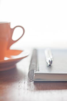 Orange coffee cup, pen and notebook on wooden table, stock photo