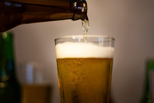 Beer is poured from the bottle into beer glass. Light fresh beer poured into glass.