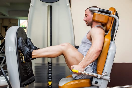 A handsome young muscular sports man doing leg press