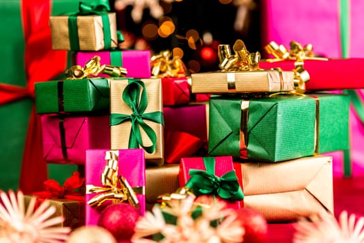 Countless Christmas gifts stacked up. Shallow depth of field. Blurred stars and baubles in front and rear. Bokeh over black background. Tightly framed. Focus on golden present with green bow.