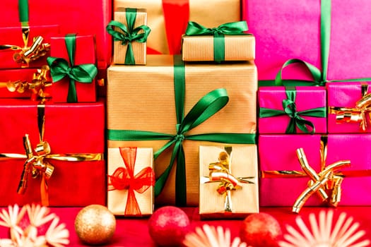 Three piles of plain Xmas presents grouped by color. Red, gold and magenta. All with bow knots. Stars and baubles on red foreground. Shallow depth of field. Vibrant colors.