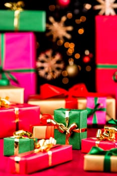 Many plain Christmas gifts arranged on a red cloth. Narrow depth of field. Mostly soft shapes in vibrant colors. Defocused straw stars and baubles over black background. Focus on central green box.