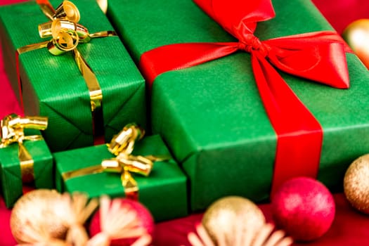Four green Christmas gifts on a red cloth. Bows in gold and crimson. Stars and baubles outside depth of field. Focus on red bowknot around largest green present. Close up, tightly framed.
