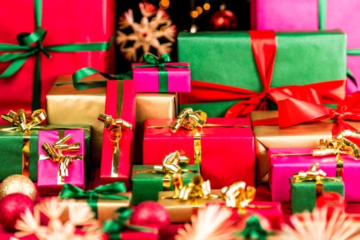 Multitude of Christmas presents waiting to be handed out. Wrapped in single colors. Red, green, gold and magenta. Blurred baubles and stars in front and back, outside the narrow depth of field.