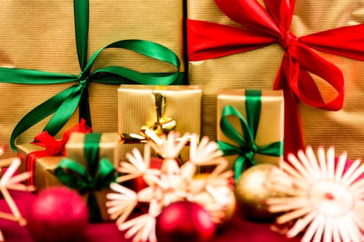Golden Christmas presents with bows in red, green and gold. Tightly framed. Shortened space. Shallow depth of field. Focus on large green bowknot in the rear. Blurred baubles and stars in front..