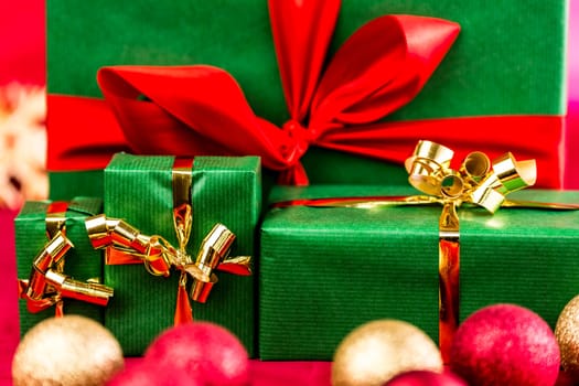 Four Christmas gifts wrapped all in green. Ribbons in gold and red. Close up. Narrow depth of field is cutting across the three golden bowknots. Blurred baubles in front and hazy straw star in rear.