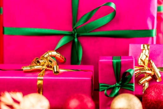 Four Christmas gifts all in plain magenta. Ribbons in gold and emerald green. Tightly framed, close up. Shortened space. Shallow depth of field. Vibrant colors. Focus on golden bow on the left.